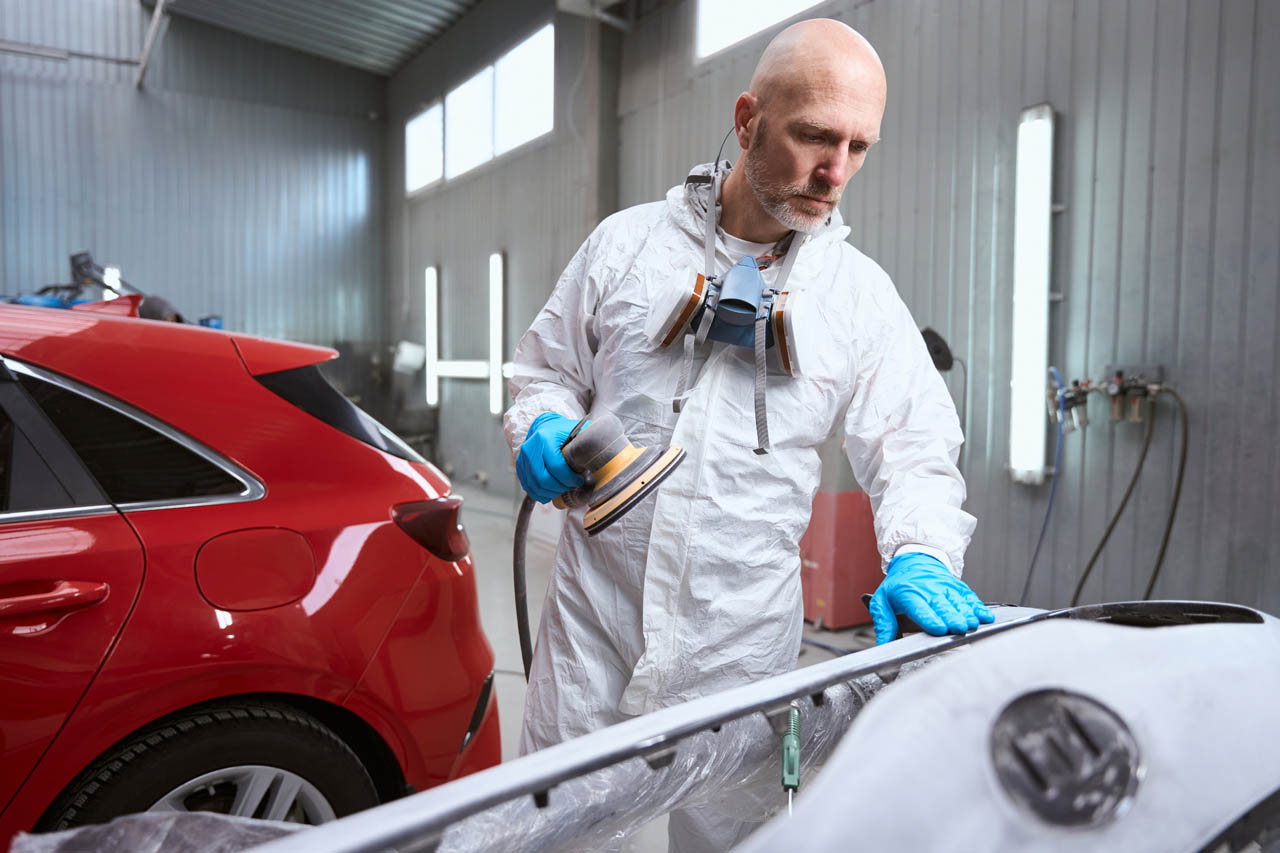 Een medewerker van een autoreparatiewerkplaats werkt aan een ongeverfde autobumper Carrosserie in Brussel